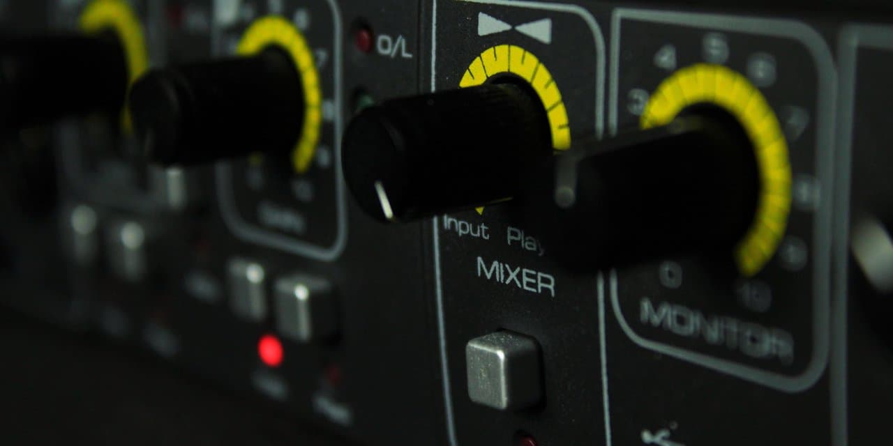 Close-up knob mixer audio berwarna kuning dengan label MIXER dan MONITOR — tahap koreksi teknis audio di studio