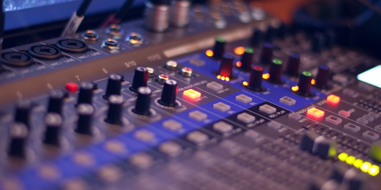 Close-up mixer audio profesional dengan lampu indikator LED menyala di ruang studio musik gelap