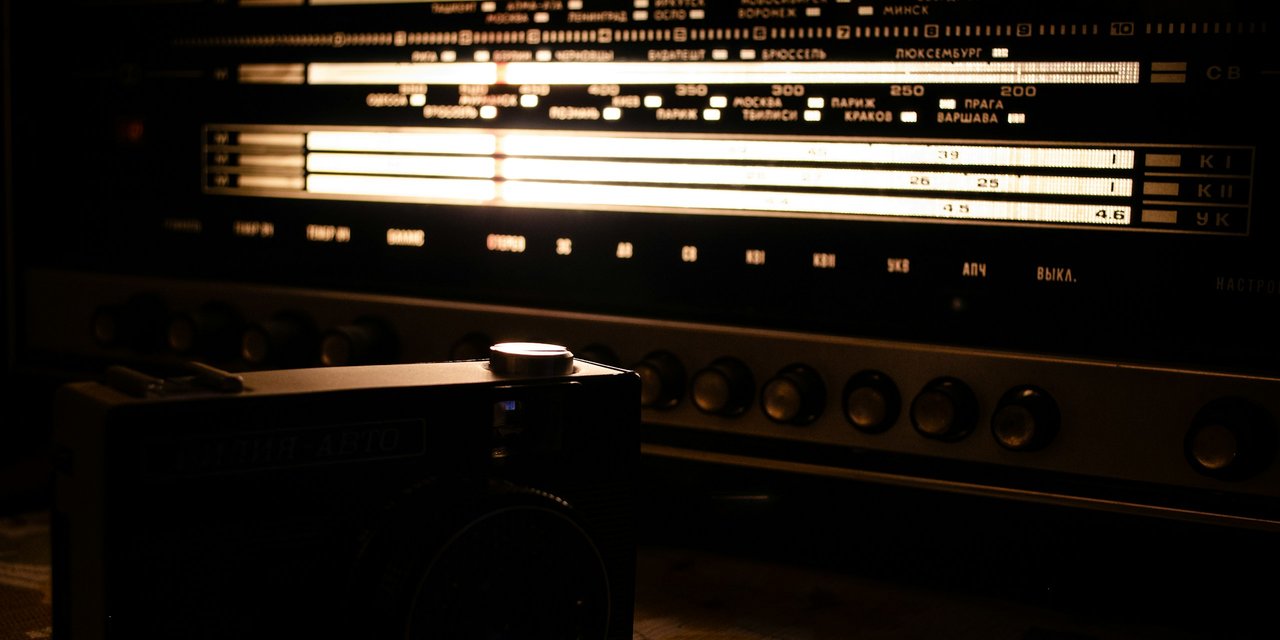Skala frekuensi radio vintage yang menyala hangat di ruangan gelap, simbol jingle iklan yang diputar di radio